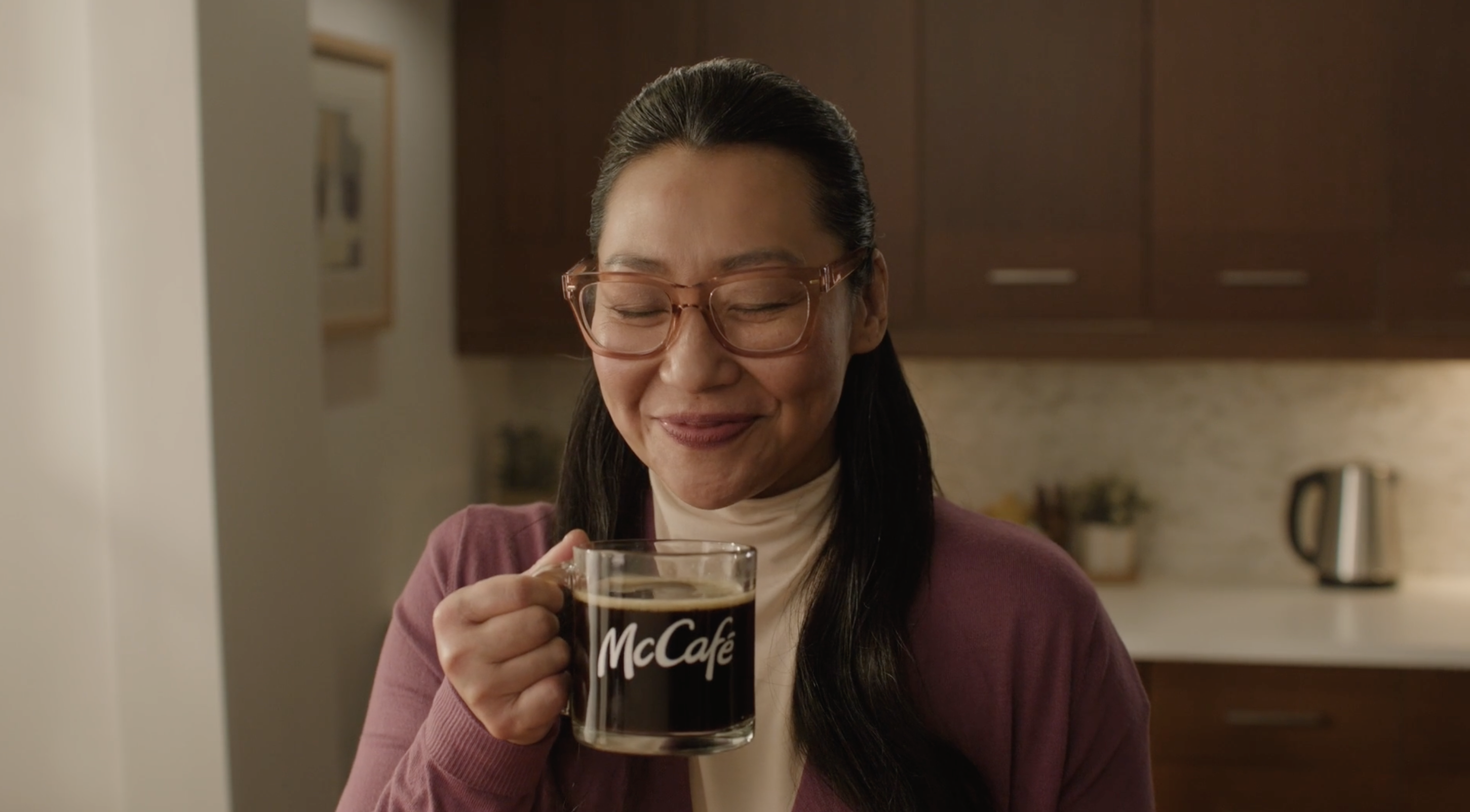 A woman holds a McCafe coffee in her hand. She smiles down at it in this commercial production for McDonald's McCafe.